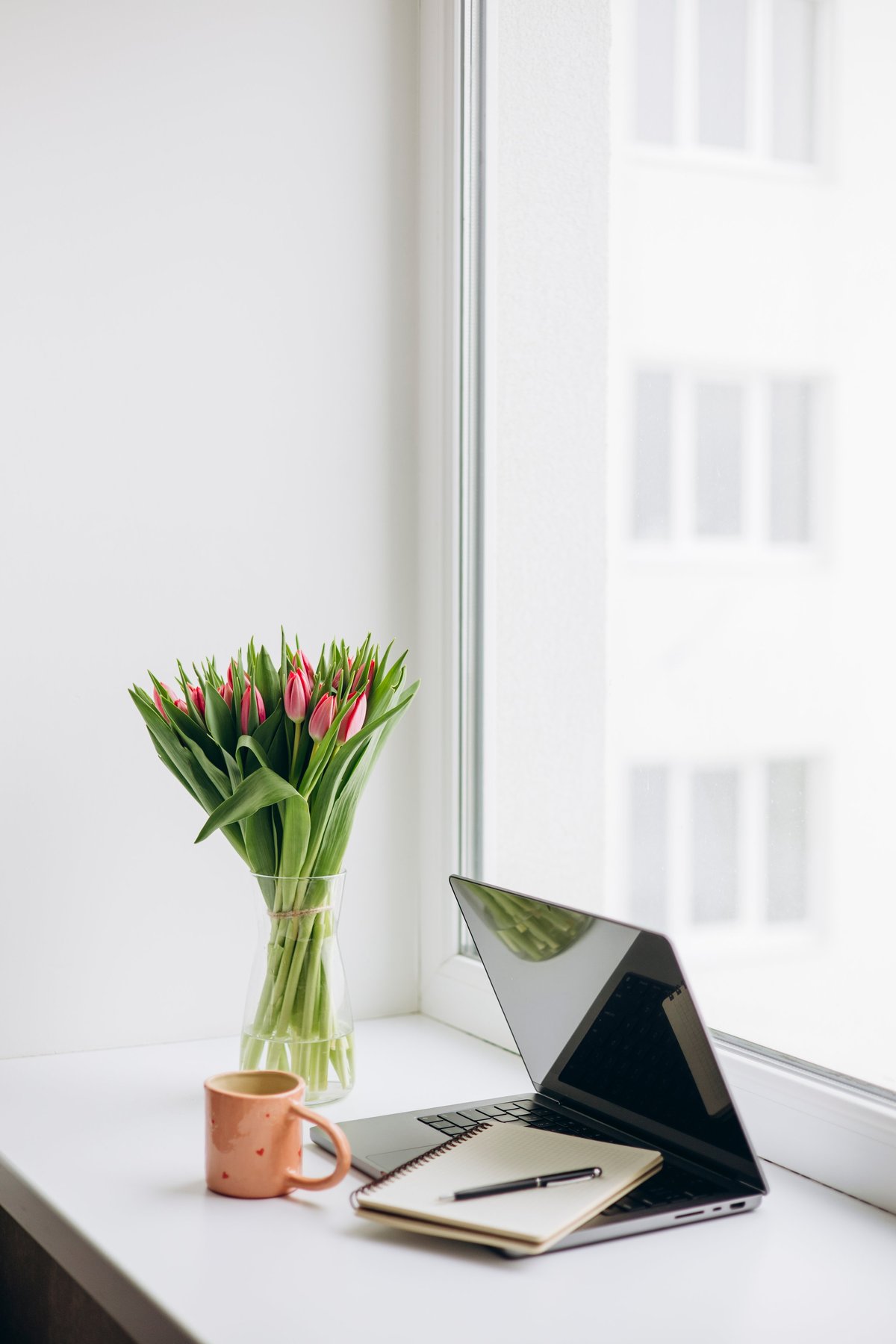 Minimal home office desk with laptop, notebook and fresh tulips by a window